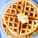 Deliciously golden waffles stacked on a plate with syrup and fruit garnish.