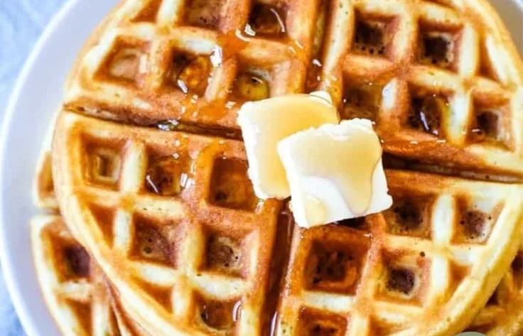 Deliciously golden waffles stacked on a plate with syrup and fruit garnish.