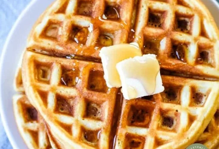 Deliciously golden waffles stacked on a plate with syrup and fruit garnish.