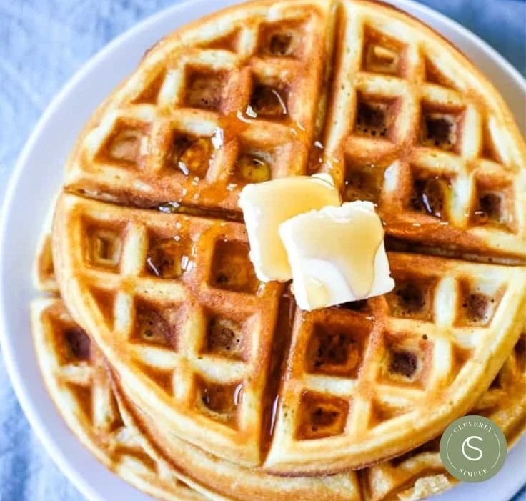Deliciously golden waffles stacked on a plate with syrup and fruit garnish.