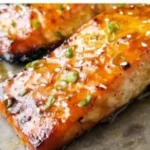 Baked orange glazed salmon dish garnished with herbs and citrus slices.