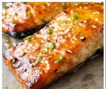 Baked orange glazed salmon dish garnished with herbs and citrus slices.
