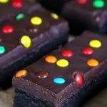 Decadent gluten free brownies topped with rich frosting on a wooden platter