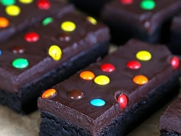 Decadent gluten free brownies topped with rich frosting on a wooden platter