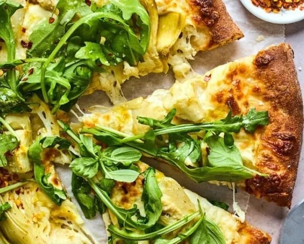 Lemon Artichoke Pizza topped with fresh arugula slice on a wooden table