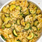 Plate of lemon zucchini pasta garnished with fresh herbs and lemon slices