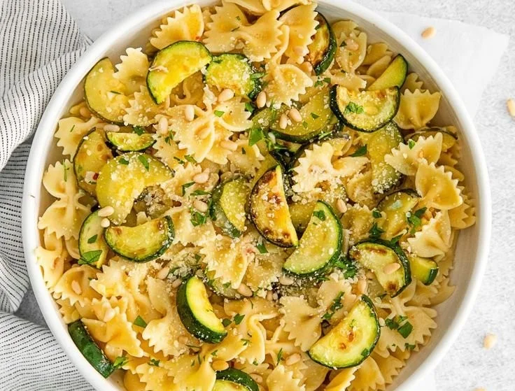 Plate of lemon zucchini pasta garnished with fresh herbs and lemon slices