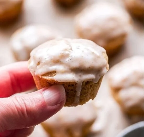 Mini chai muffins topped with vanilla bean glaze on a wooden table.