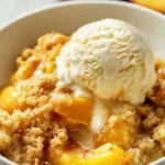 Delicious Peach Dump Cake dessert served in a bowl with fresh peach slices.
