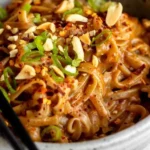 Bowl of spicy peanut butter noodles with vegetables and herbs
