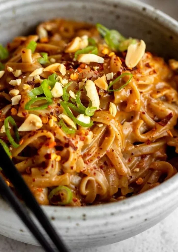 Bowl of spicy peanut butter noodles with vegetables and herbs