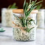 Homemade rosemary salt in a glass jar with fresh rosemary sprigs