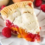 Slice of peach raspberry pie topped with whipped cream on a plate