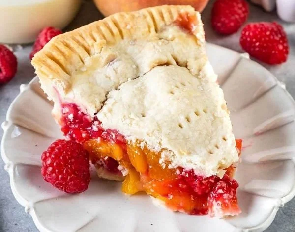 Slice of peach raspberry pie topped with whipped cream on a plate