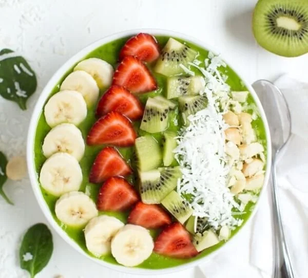 Delicious tropical green smoothie bowl topped with fresh fruits and seeds.