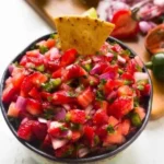 Bowl of fresh strawberry jalapeño salsa with ingredients on the side.
