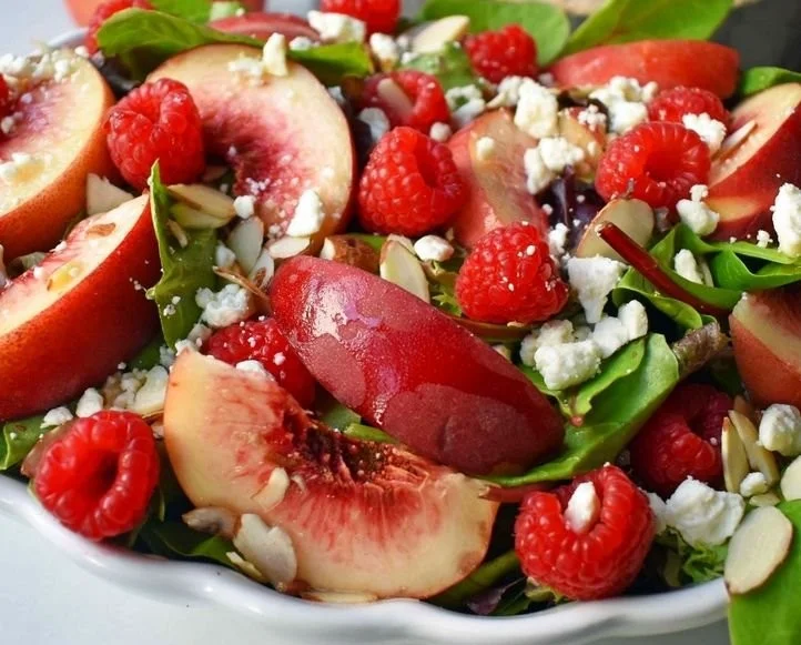 White peach raspberry almond salad in a vibrant bowl, garnished with fresh mint.