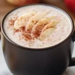 A steaming cup of apple chai latte garnished with cinnamon and apple slices.