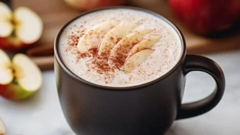 A steaming cup of apple chai latte garnished with cinnamon and apple slices.