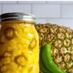A jar of homemade pineapple jalapeño pickles on a wooden table.