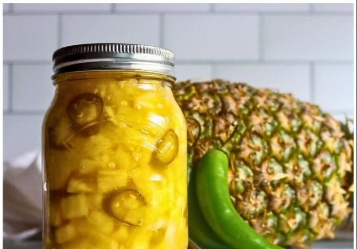 A jar of homemade pineapple jalapeño pickles on a wooden table.