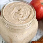 Homemade apple cinnamon sugar scrub in a glass jar with a spoon.