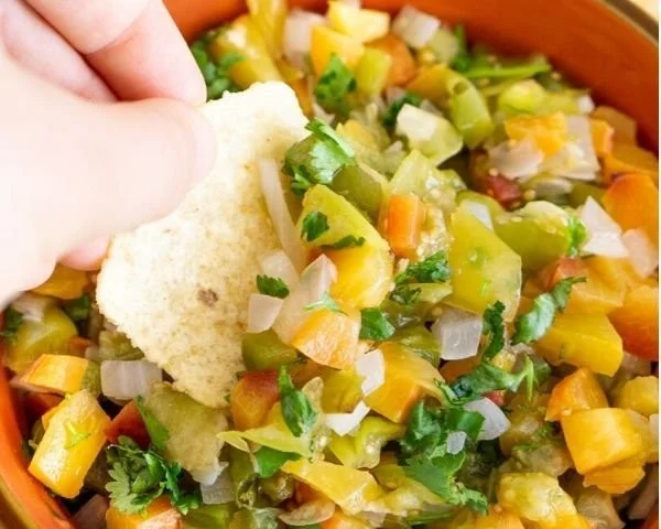 Roasted tomatillo and peach salsa served in a bowl with fresh herbs