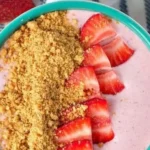 Strawberry cheesecake smoothie bowl topped with fresh strawberries and granola