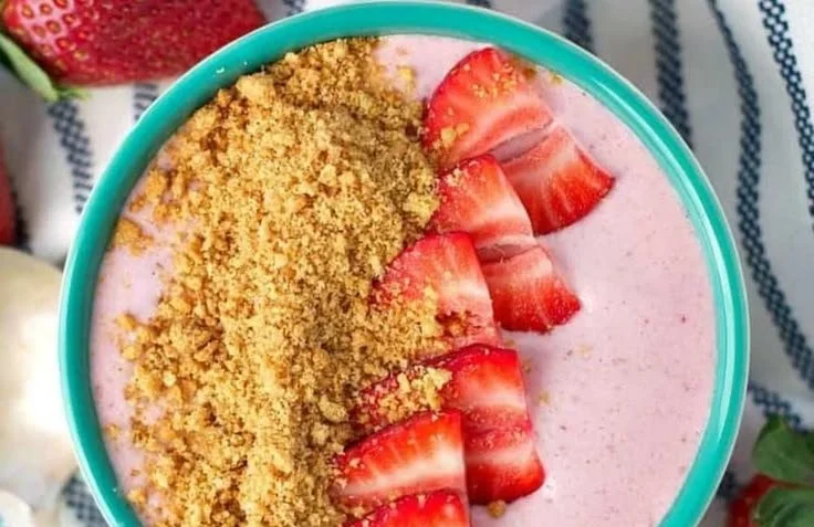 Strawberry cheesecake smoothie bowl topped with fresh strawberries and granola