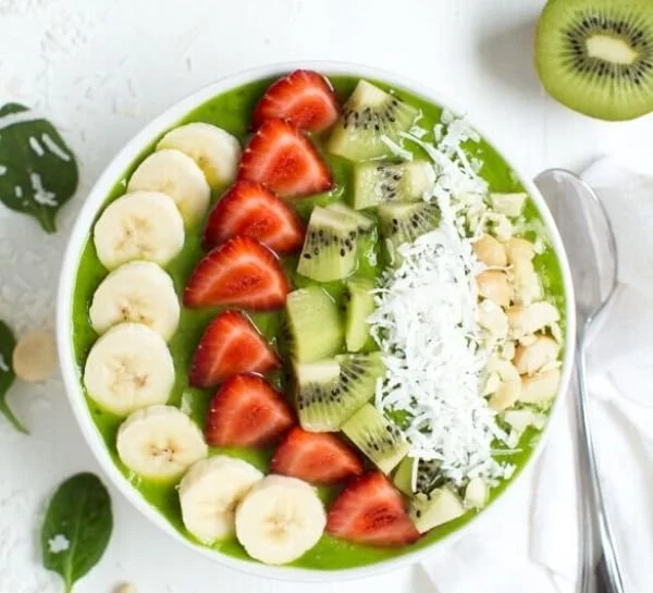 Tropical green smoothie bowl topped with fresh fruits and seeds